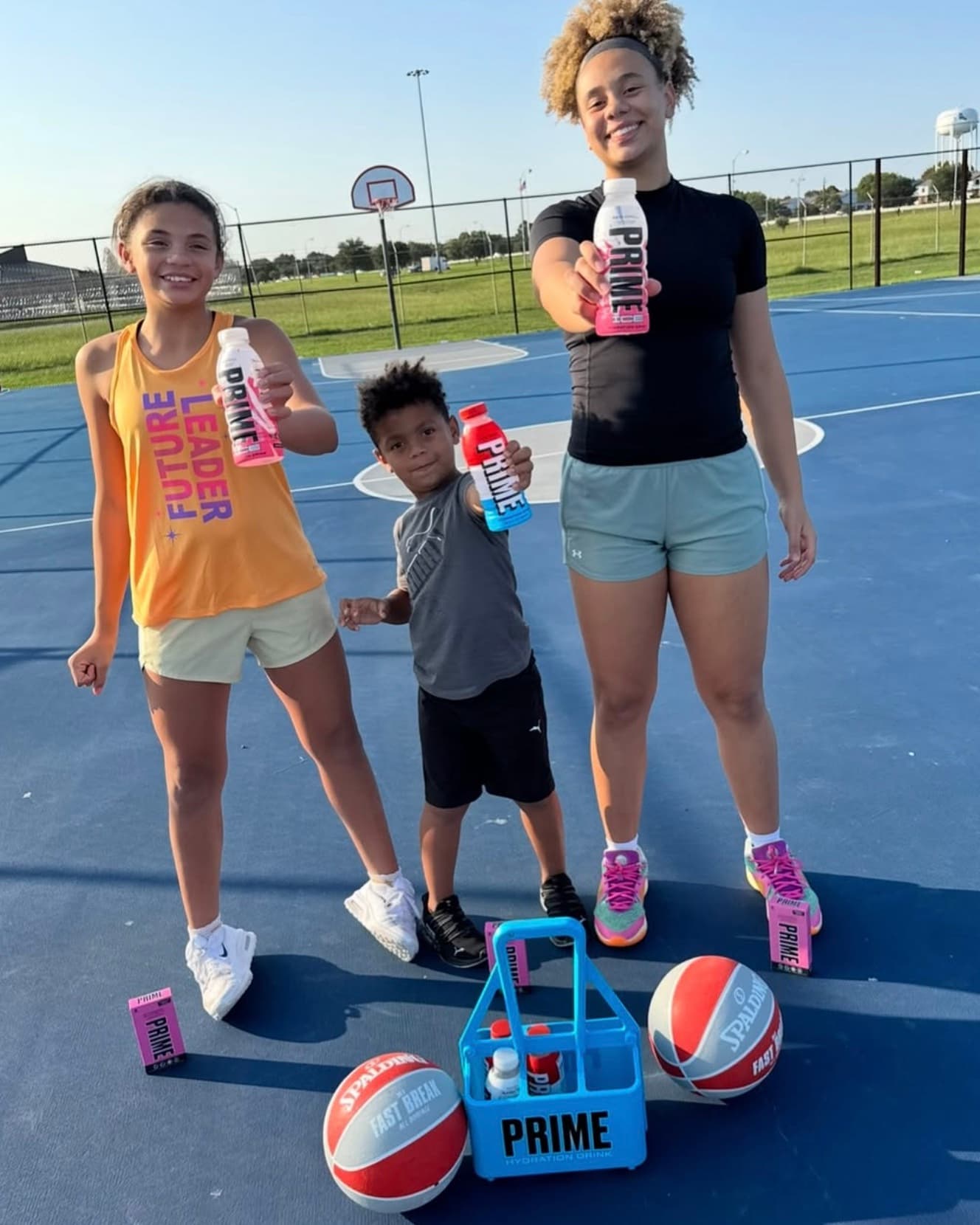 Three young athletes smiling on an outdoor basketball court after a session